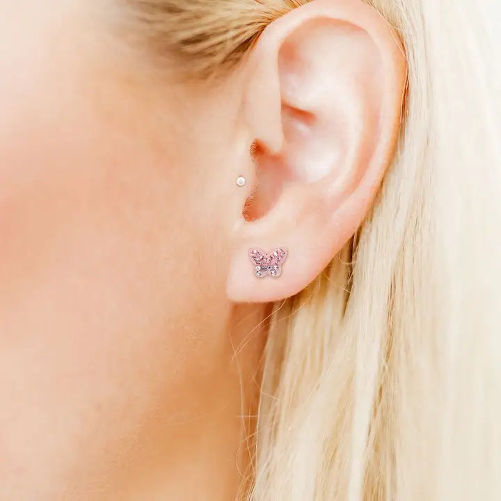 Close-up of an ear wearing a pink heart-shaped earring with small clear stones.