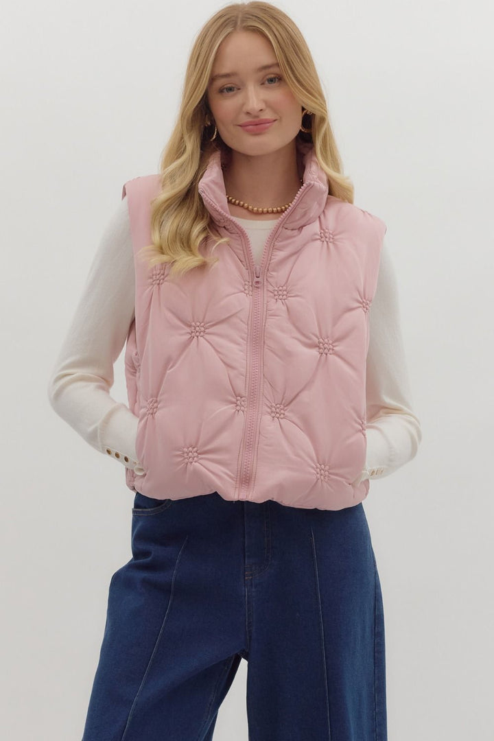 Woman wearing a pink quilted vest over a white long-sleeve shirt and blue pants on a white background