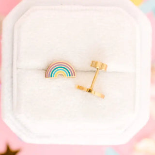 A pair of gold rainbow stud earrings displayed on a white jewelry box cushion against a soft pink background.
