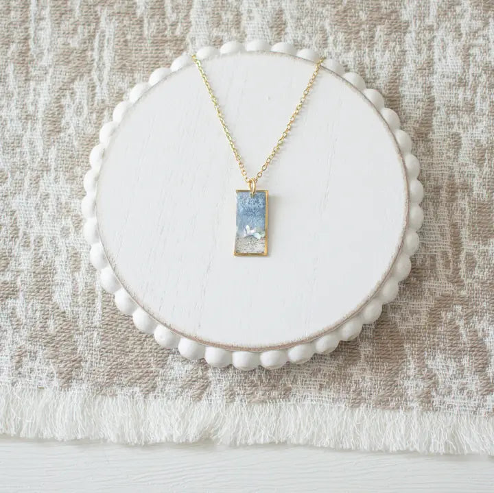 Necklace with a pendant on a white circular stand against a textured beige background