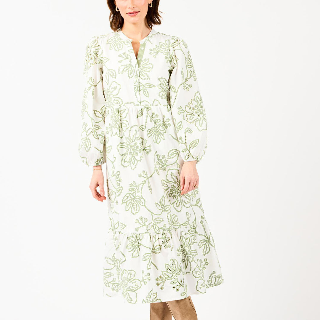 Woman wearing a white dress with green floral embroidery on a white background