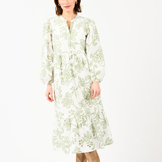 Woman wearing a white dress with green floral embroidery on a white background