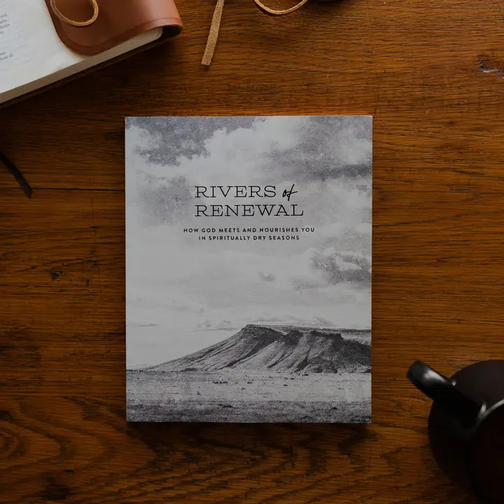 Book titled 'Rivers of Renewal' on a wooden surface with a teacup and notebook.