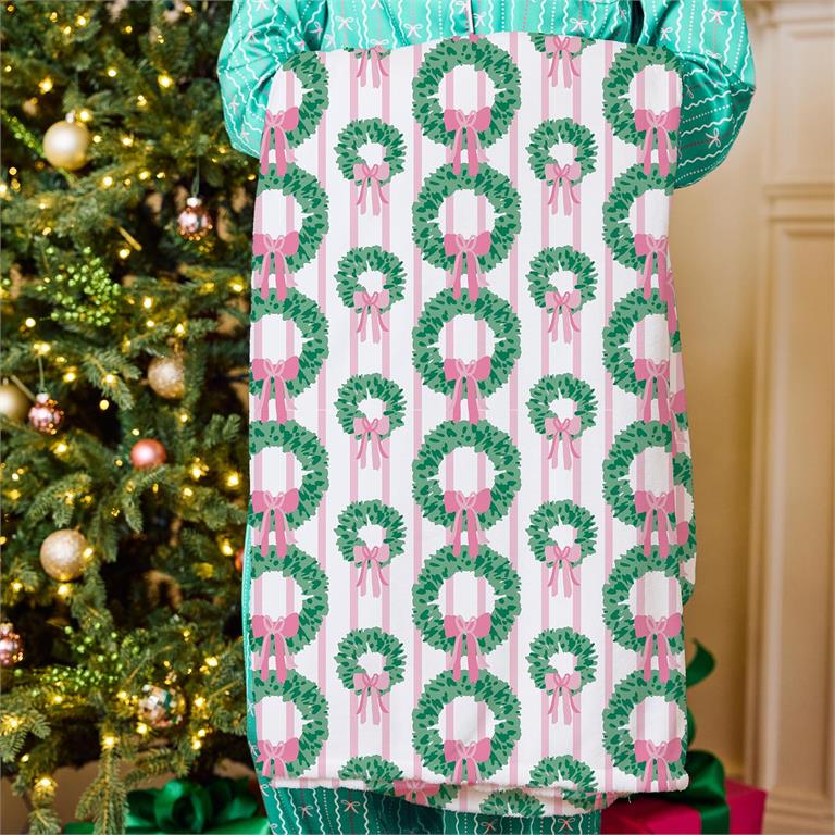 Person wearing a festive apron with Christmas wreath pattern in front of a decorated tree.
