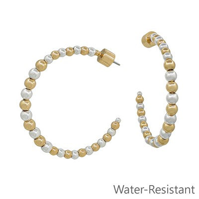 Pair of gold and white beaded hoop earrings on a white background with &