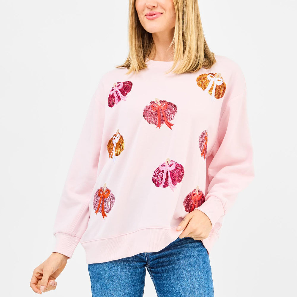 Person wearing a pink sweatshirt with colorful pumpkin patterns on a white background
