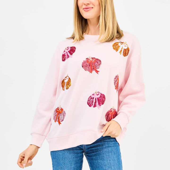 Person wearing a pink sweatshirt with colorful pumpkin patterns on a white background