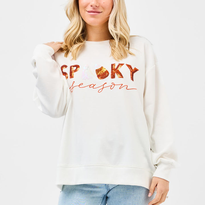 Person wearing a white sweatshirt with 'Spooky Season' text and pumpkin graphics on a white background