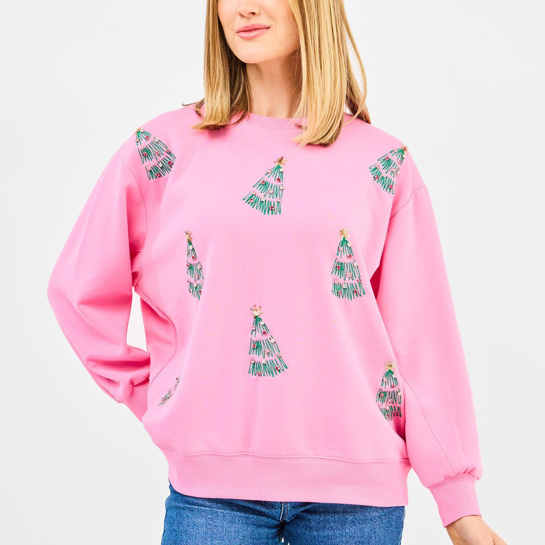 Person wearing a pink sweatshirt with green tree patterns on a plain background