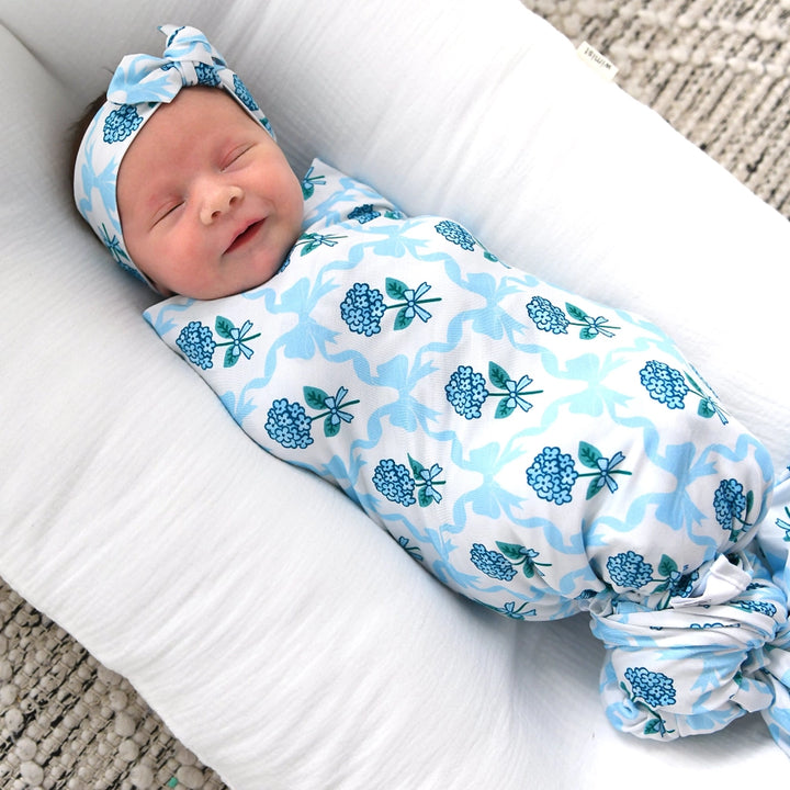 Newborn baby swaddled in a blue floral patterned blanket on a white surface.