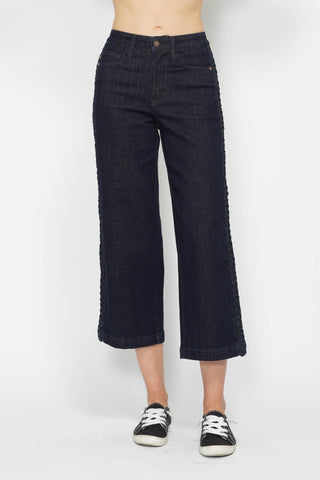 Person wearing dark blue jeans and black sneakers on a white background