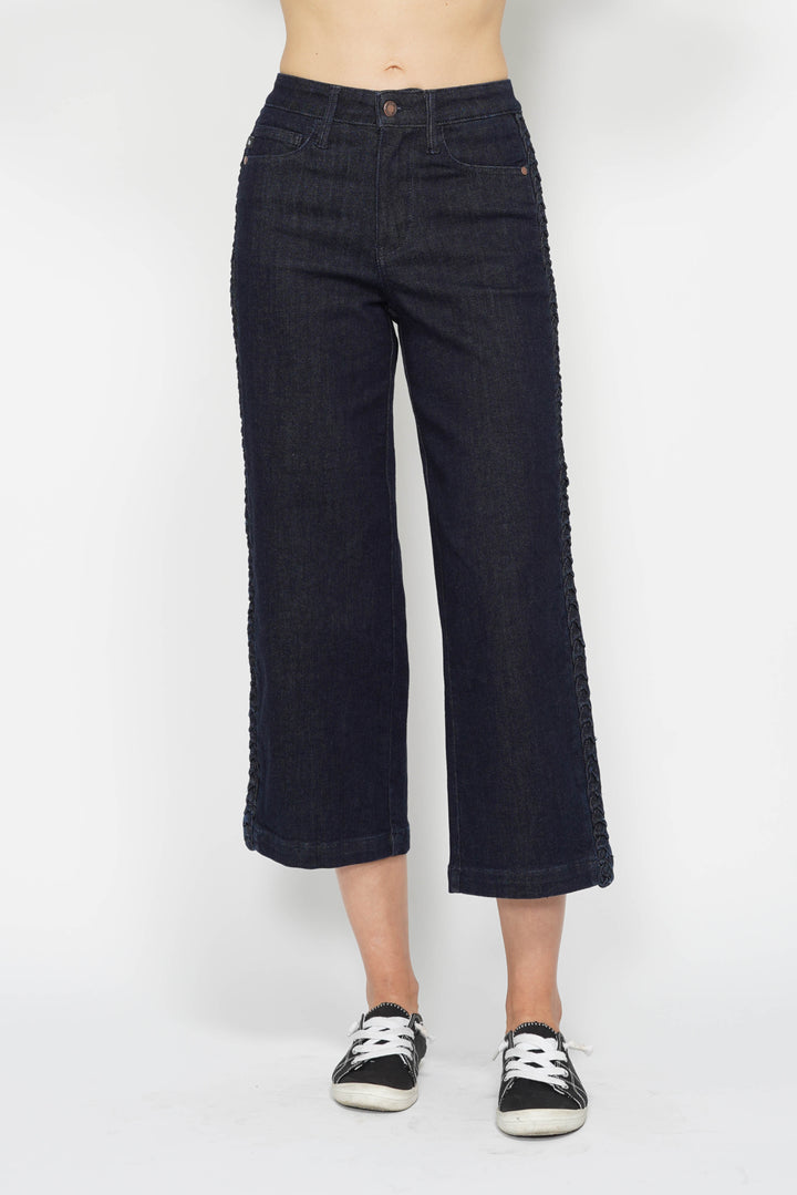 Person wearing dark blue jeans and black sneakers on a white background