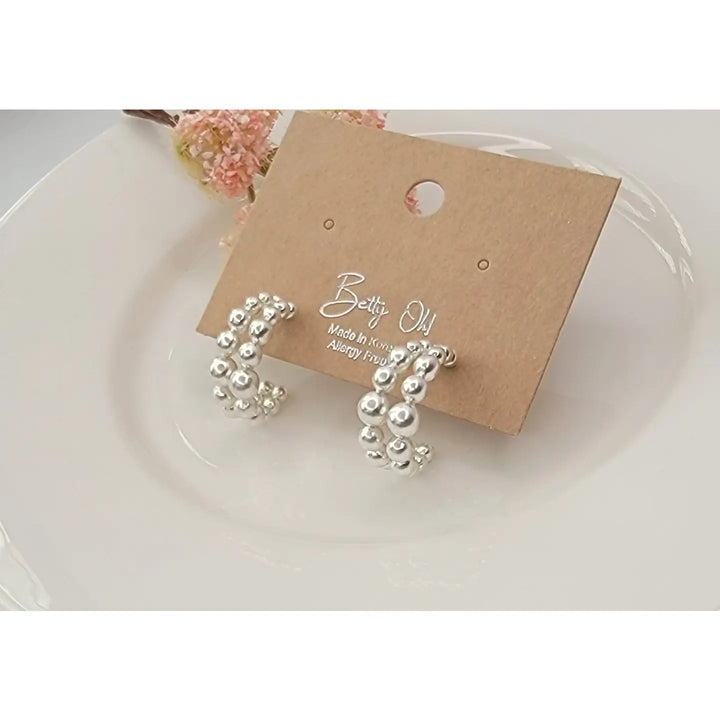 Silver beaded earrings on a brown card with 'Betty Oh' branding, placed on a white surface.