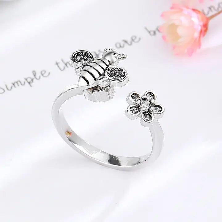 Silver ring with bee and flower designs on a light background