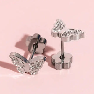 Silver butterfly stud earrings with flower-shaped posts, shown on a soft pink background.