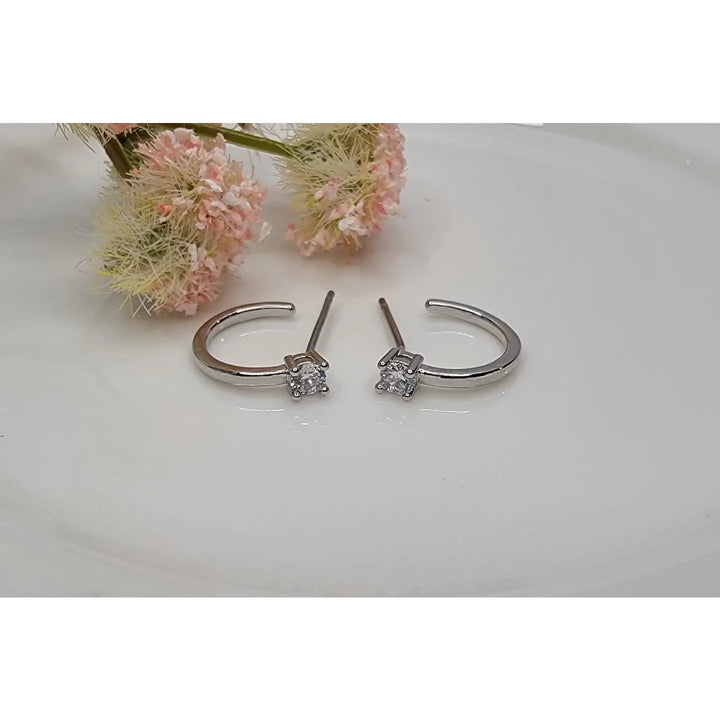 Silver hoop earrings with clear gemstones on a white surface with pink flowers in the background.