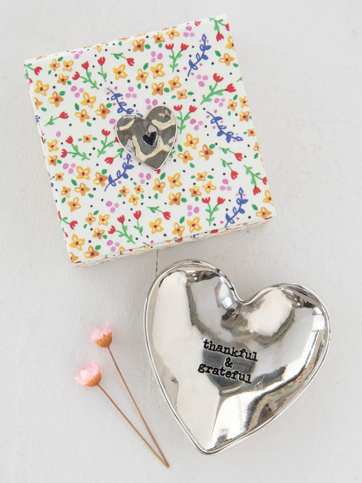 Heart-shaped silver trinket dish with 'thankful & grateful' text, next to a floral-patterned box on a light background.