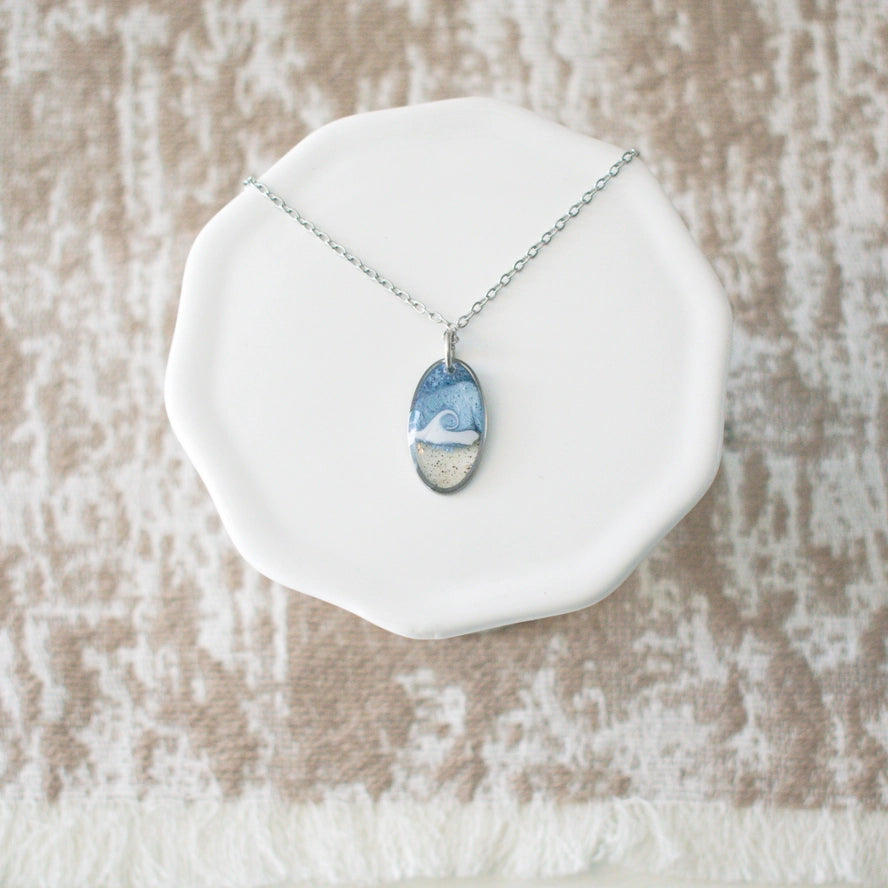 Necklace with a scenic pendant on a white dish against a textured beige background