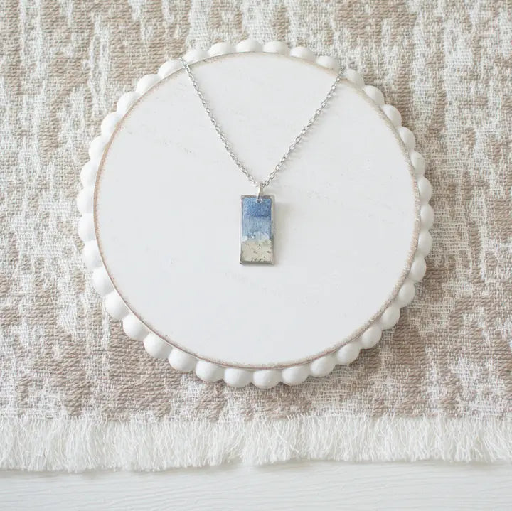 Necklace with a pendant on a white circular stand against a textured beige background