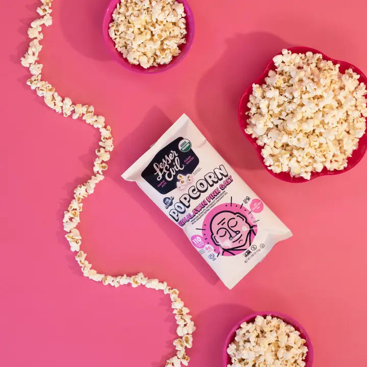 Popcorn kernels, bowls of popcorn, and a popcorn bag on a pink background