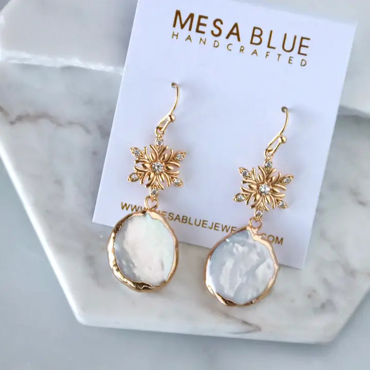Gold and white earrings on a Mesa Blue branded card with marble background
