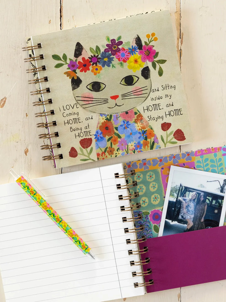 Notebook with a colorful cat illustration on the cover, surrounded by photos and a pen.