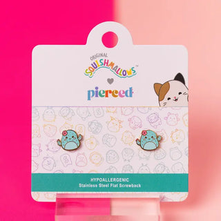 A pair of Squishmallows branded stud earrings by Pierced, displayed on their original white cardboard hanger card. The earrings are light blue with a small pink bow and are shown against a vibrant pink and peach gradient background.