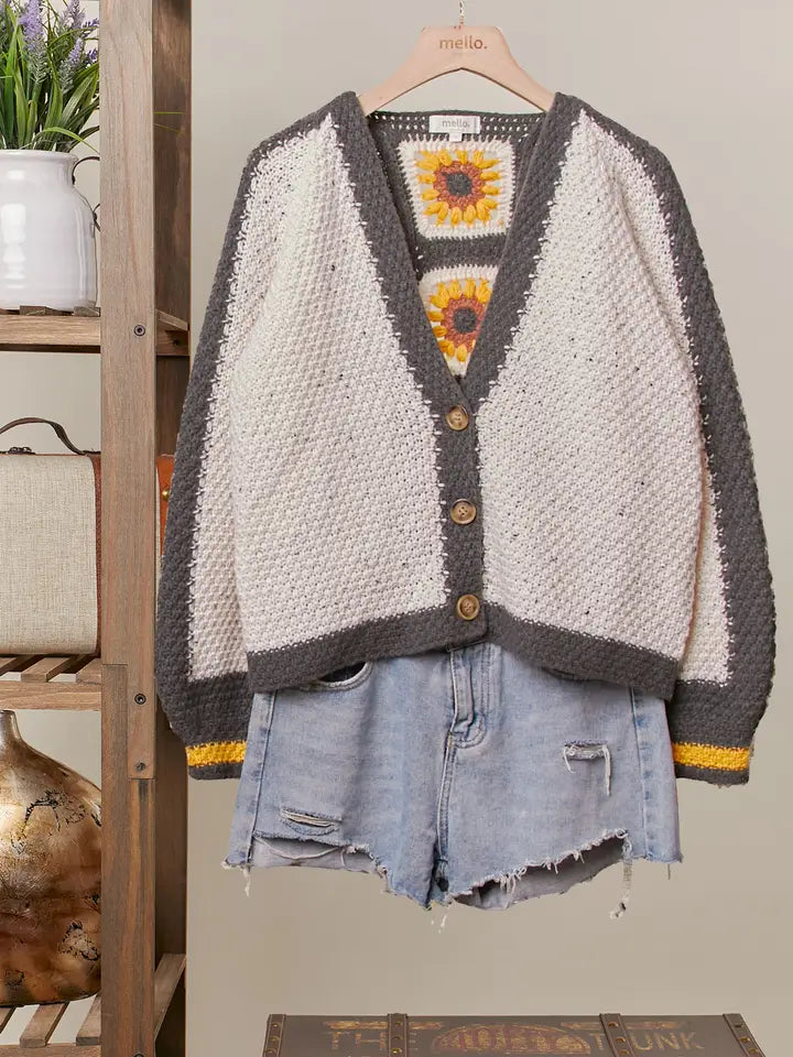 Cardigan with sunflower design and denim shorts on a wooden shelf.