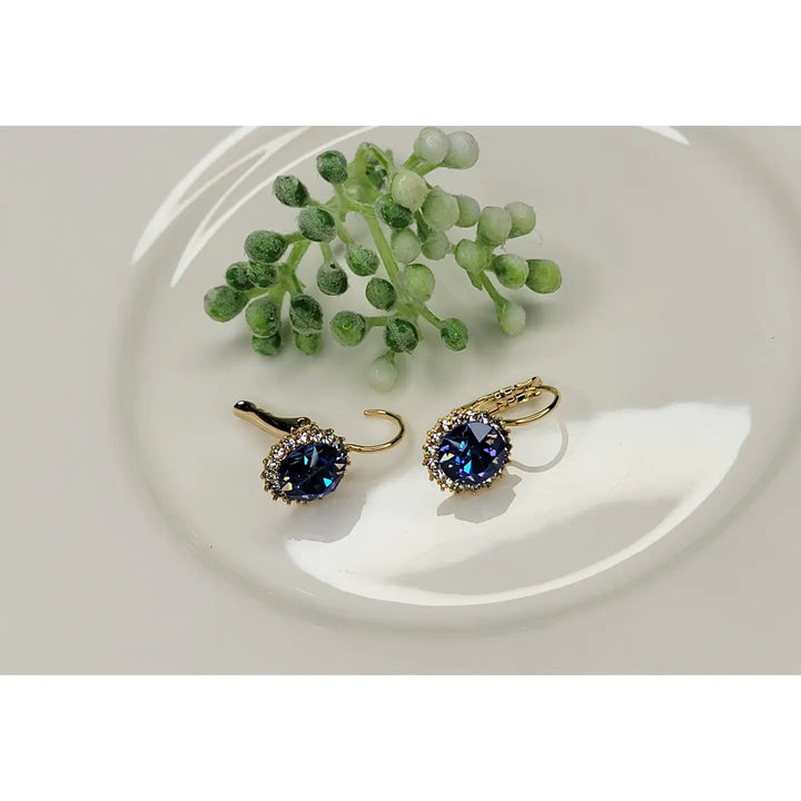 Pair of gold earrings with blue gemstones on a white plate with green leaves.