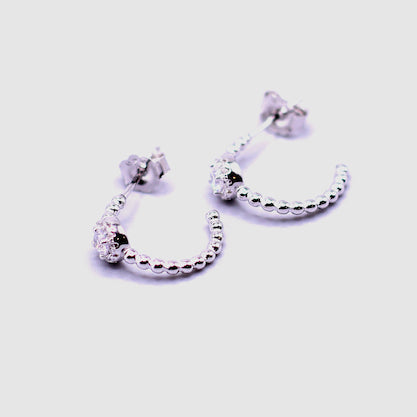 Pair of silver hoop earrings with beaded accents on a light purple background