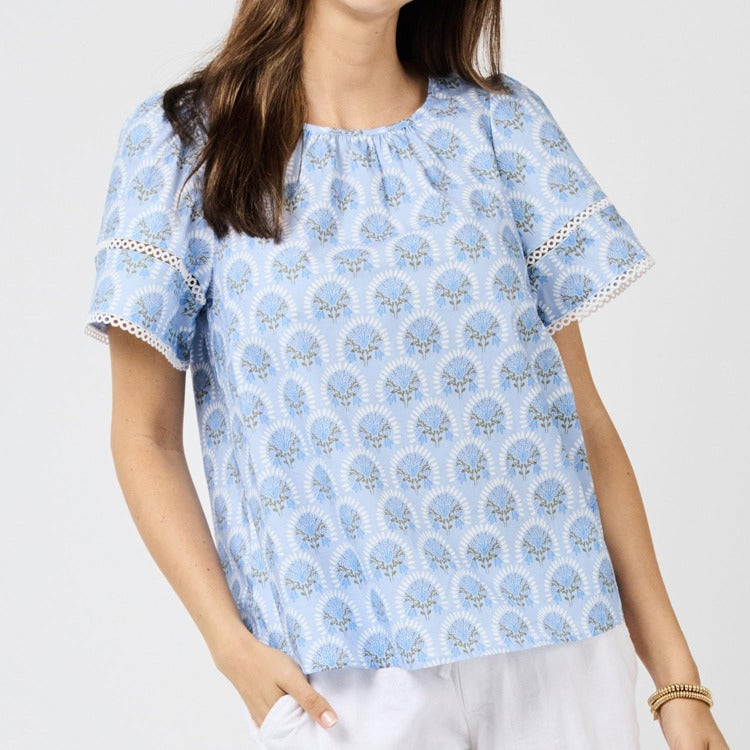 Woman wearing a blue patterned blouse with white pants on a light gray background