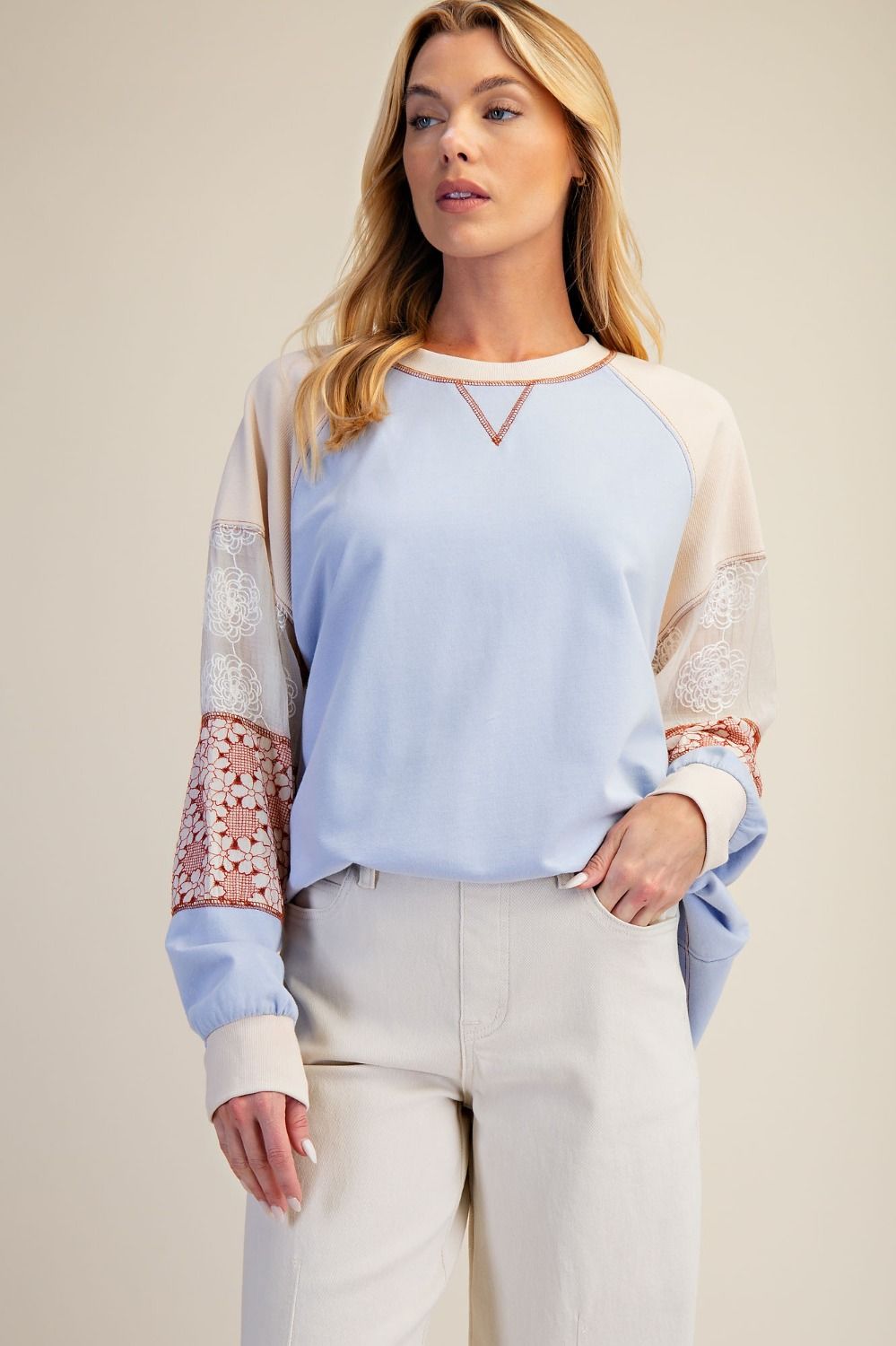 Woman wearing a light blue sweater with lace sleeves against a beige background