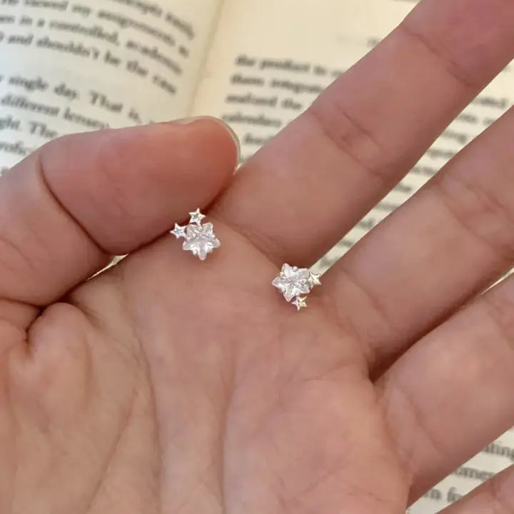 Silver star-shaped earrings held between fingers with a book in the background