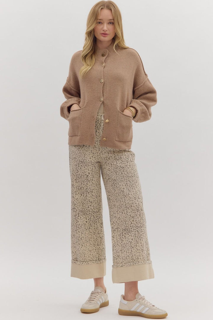 Woman wearing a beige cardigan and patterned pants on a white background