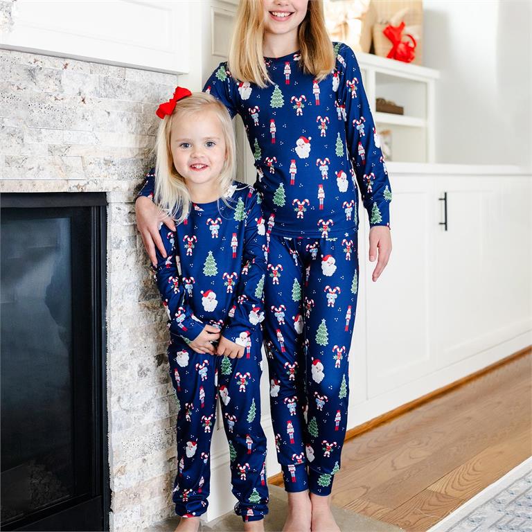 Two children wearing matching blue pajamas with Christmas patterns standing in a room.