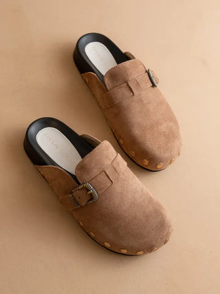 Pair of brown suede slippers with a buckle on a beige background