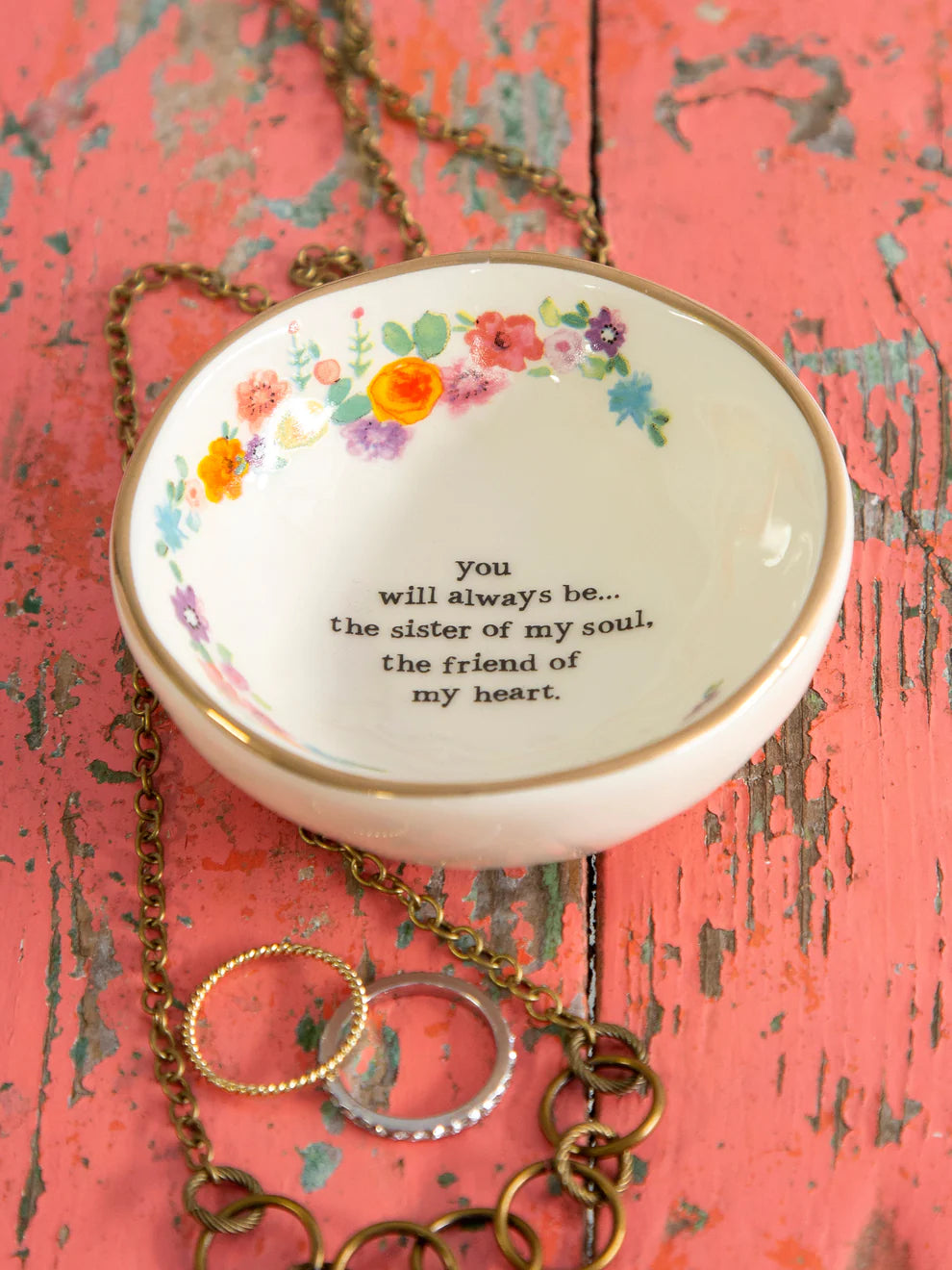 Decorative jewelry dish with floral design and text on a pink wooden surface