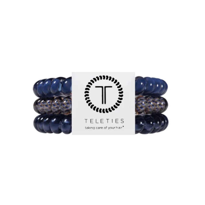 Three Teleties hair stretch bands in navy blue and speckled gray, wrapped around a white paper band with the Teleties logo.