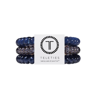 Three Teleties hair stretch bands in navy blue and speckled gray, wrapped around a white paper band with the Teleties logo.