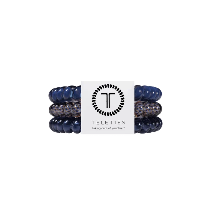 Three Teleties hair stretch bands in navy blue and speckled gray, wrapped around a white paper band with the Teleties logo.