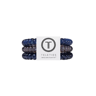 Three Teleties hair stretch bands in navy blue and speckled gray, wrapped around a white paper band with the Teleties logo.