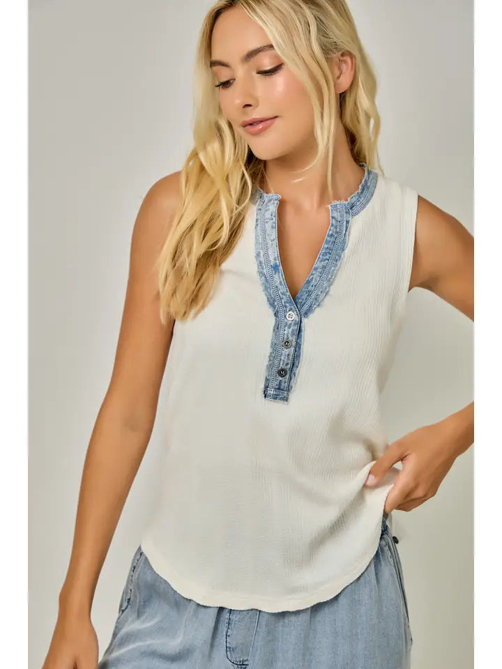 Woman wearing a sleeveless top with denim trim against a plain background