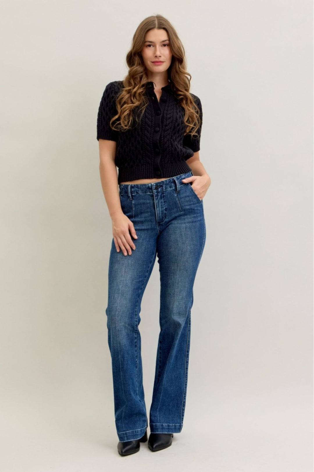 Woman wearing a black cropped top and blue jeans on a plain background