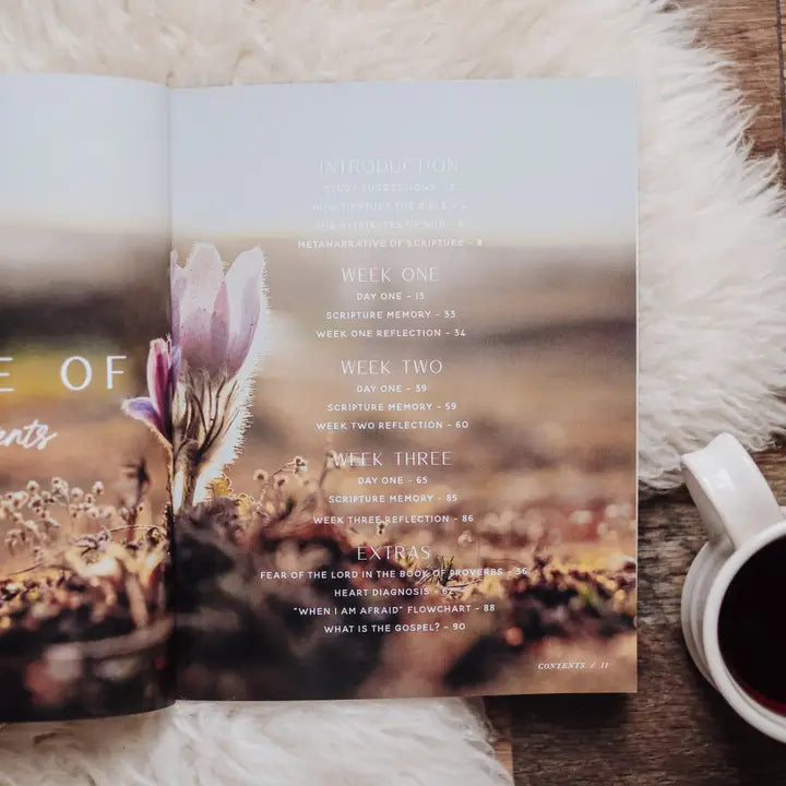 Open book with nature-themed design on a wooden surface with a cup of coffee.