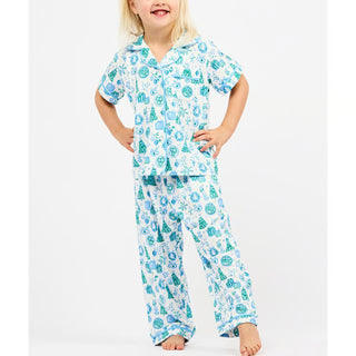 kid wearing white short sleeve and pants pajama set with green and blue christmas icon design. 