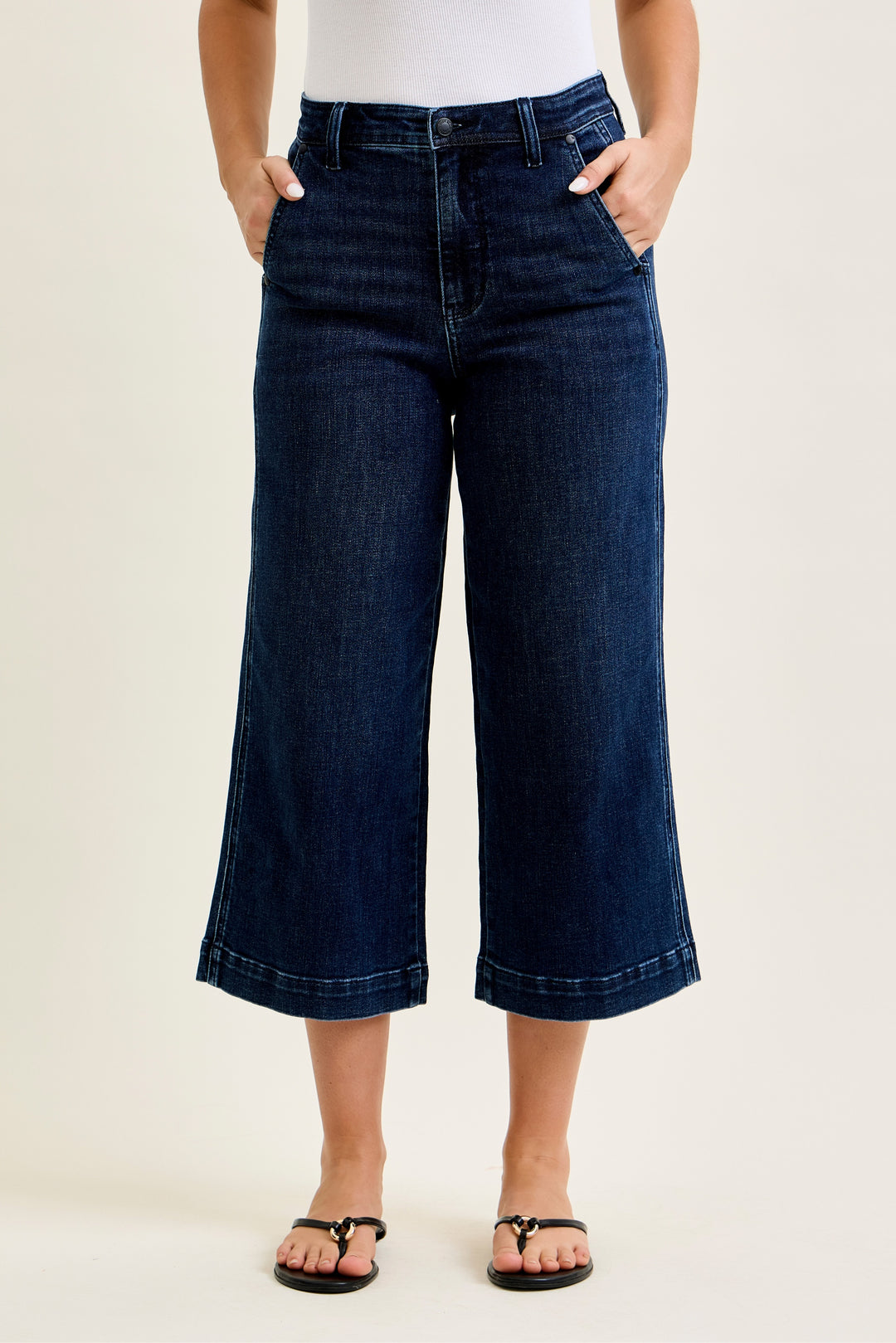 Person wearing dark blue wide-leg jeans on a beige background