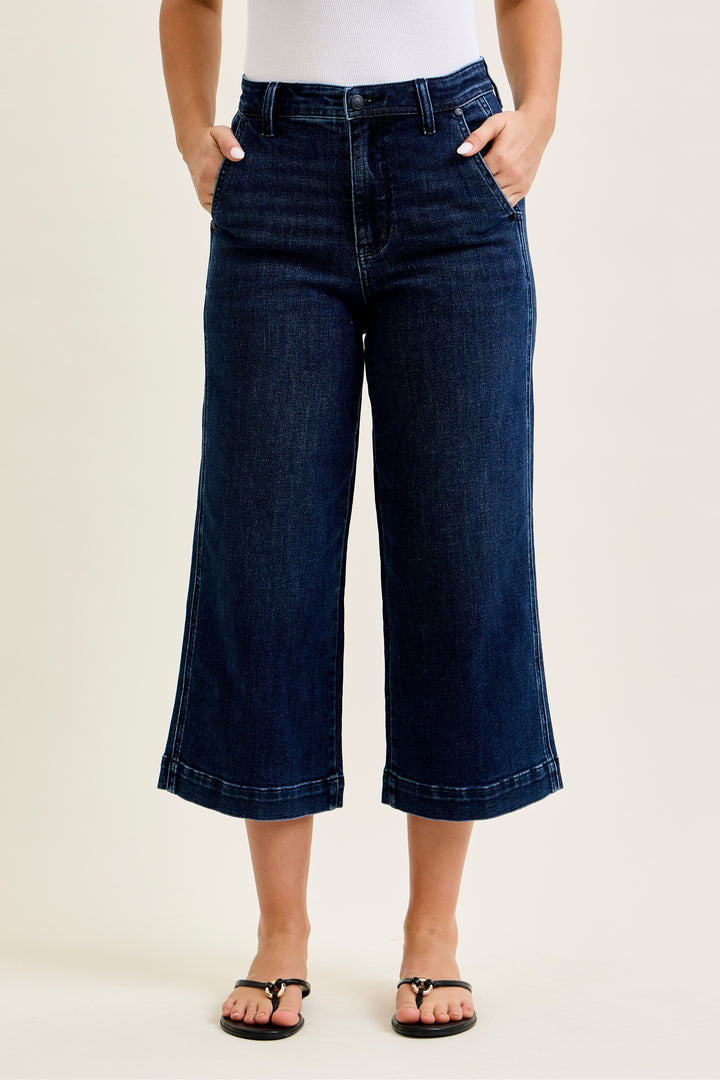 Person wearing dark blue wide-leg jeans on a beige background