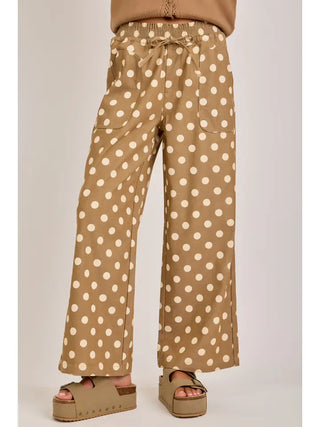 A person wearing tan wide-leg drawstring pants with a white polka dot pattern, paired with matching platform sandals, shown from the waist down against a light gray studio background.