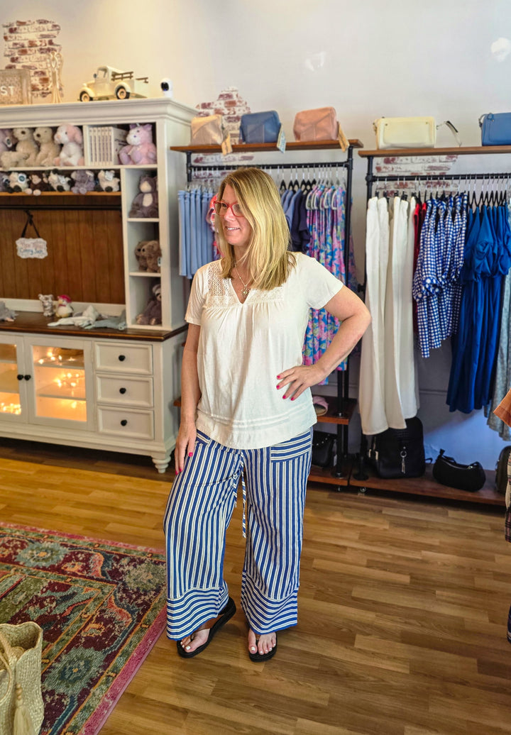 Woman standing in a clothing store with racks of clothes and shelves in the background.