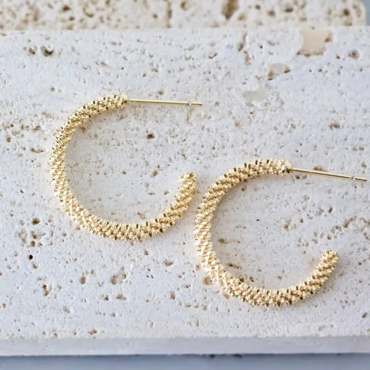 Gold hoop earrings on a textured stone surface